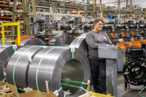 Metals industry employee standing next to rolls of high carbon steel on the shop floor.