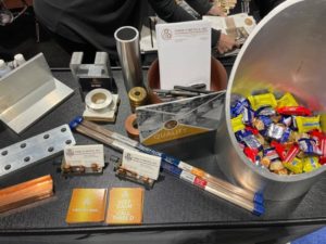 Various Three D Metals branded items on a table including business cards, parts, and candy.